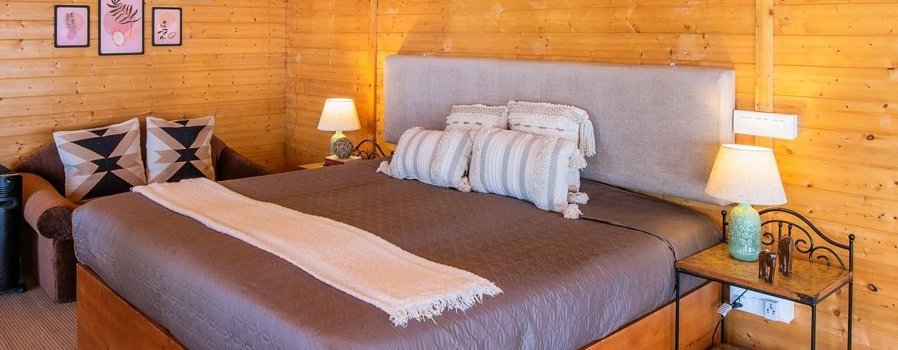 An image of a bedroom with double size bed frames hanging on the all, bedside table on either side, and a light hanging from the ceiling - Avalon Cottages, Kanatal