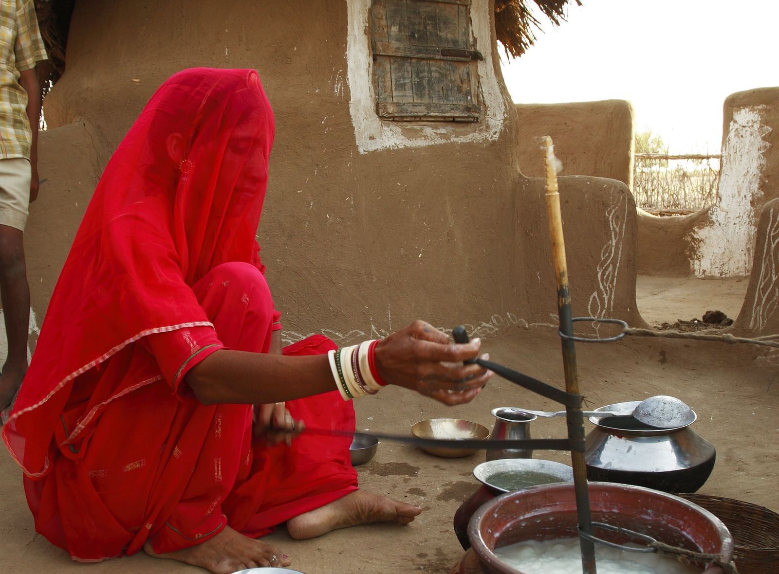A lady cooking food in a village with her mud house next to her