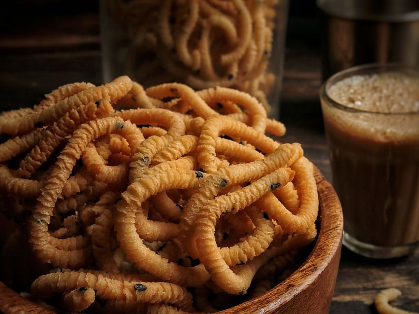 a bowl with murukku inside it next to a glass of tea
