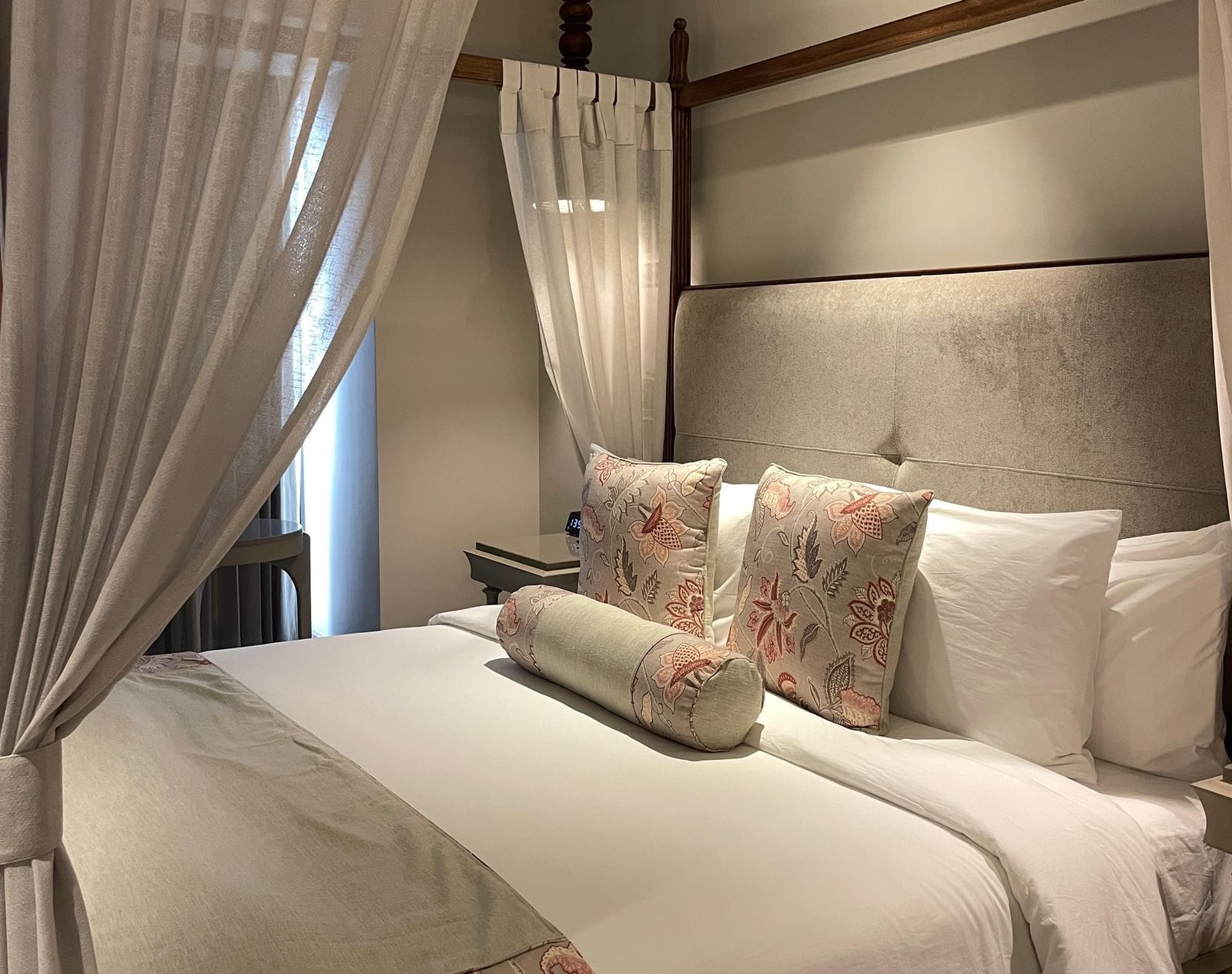 A side view of the four-poster bed in a Premium King Room at The Evren, Vagator. The bed is dressed with a bed runner and decorative pillows, and the white curtains are tied back, letting in natural light.