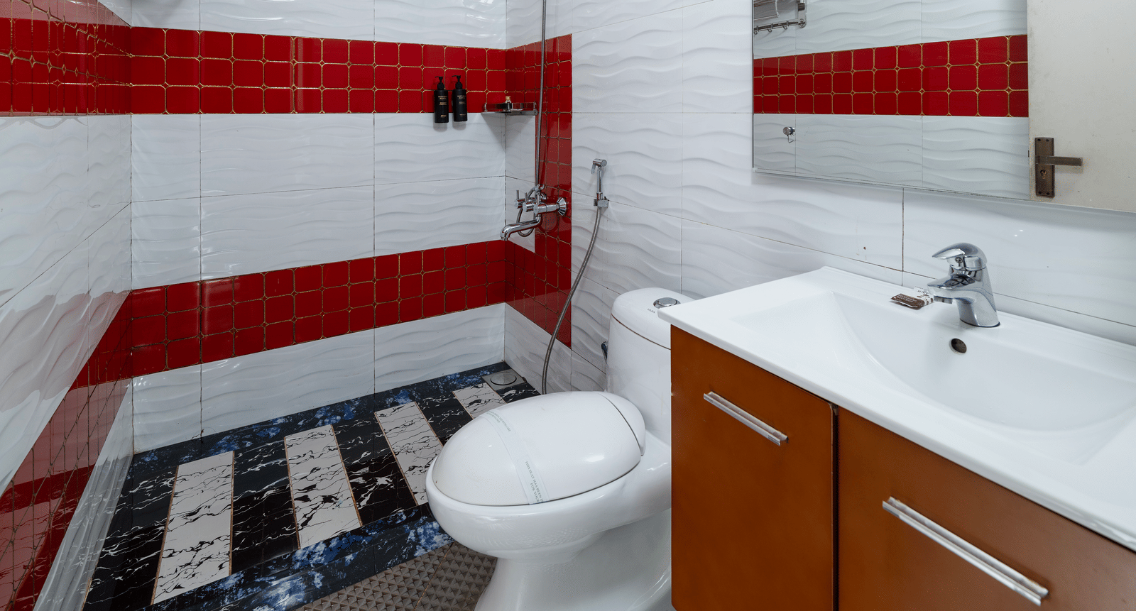 The modern bathroom for the Deluxe Non-AC Room at Parakkat Nature Hotel and Resorts, Munnar is featuring contrasting tiled walls, a sink vanity with storage, a mirror, and a toilet.