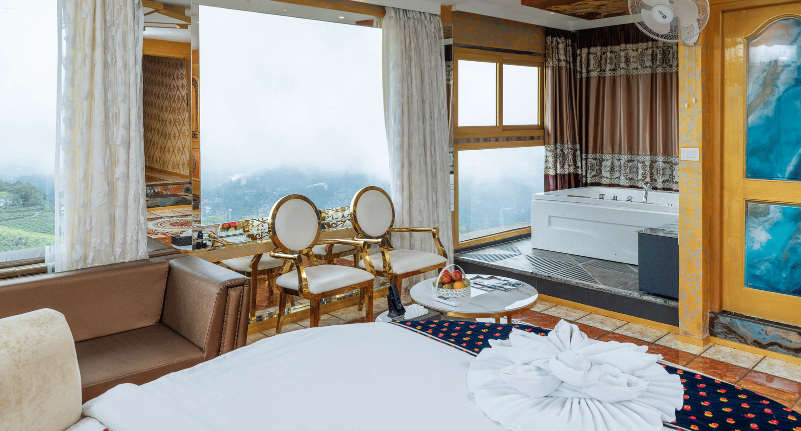 A wide interior view of the Jacuzzi 180-degree Suite at Parakkat Nature Hotel and Resorts, Munnar, featuring a large round bed, unique gold-accented ceiling design, and panoramic windows overlooking the landscape.