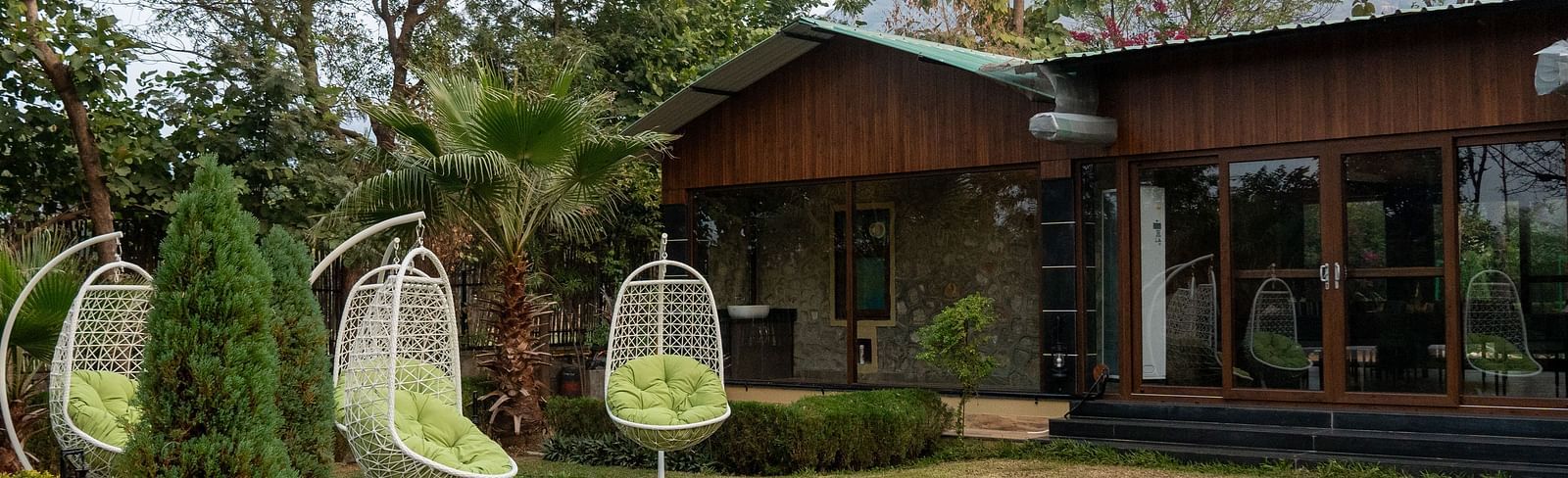 The expansive garden of Aamaghati Jungle Retreat Ranthambore featuring swings and a charming building.