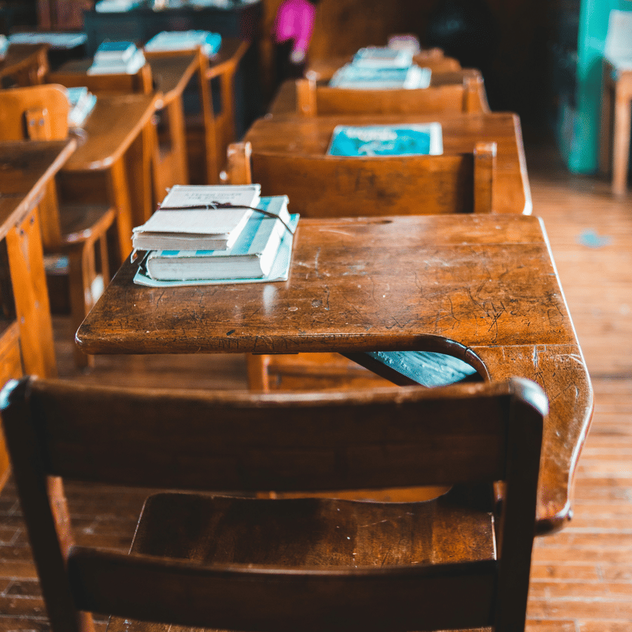 A classroom with wooden desks, books, and students in the background
