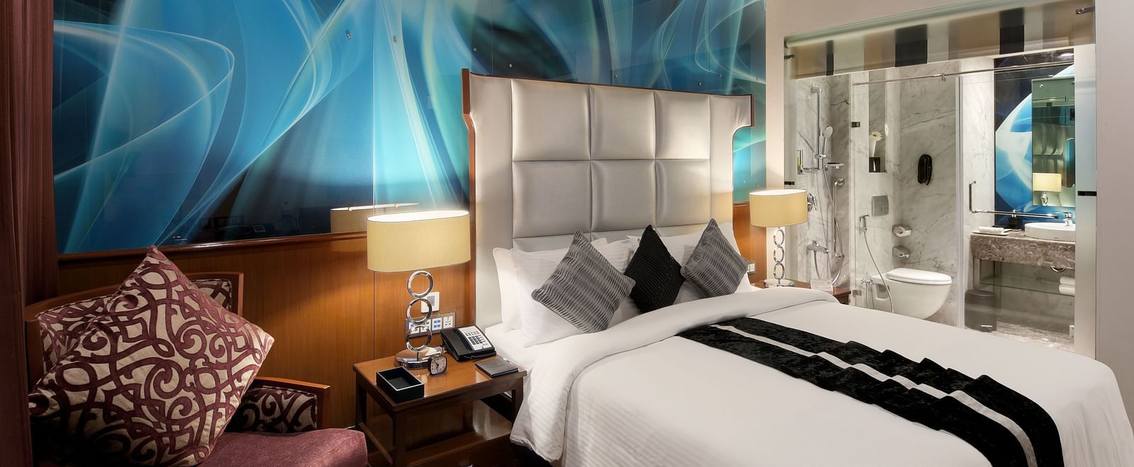 Spacious room with a large bed and cushioned sofa beside it, with a washroom in the background at The Elanza Hotel.