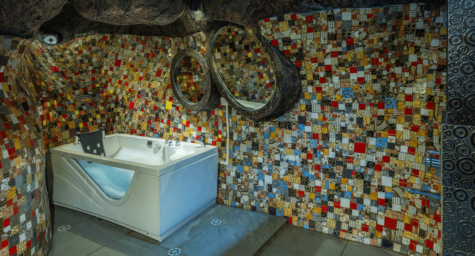The bathroom in the Cave Room at Parakkat Nature Hotel and Resorts, Munnar, featuring a deep-soaking tub built into the floor and textured wall tiling.