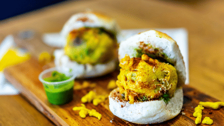 A couple of vada pav kept on a wooden surface with a chutney in between