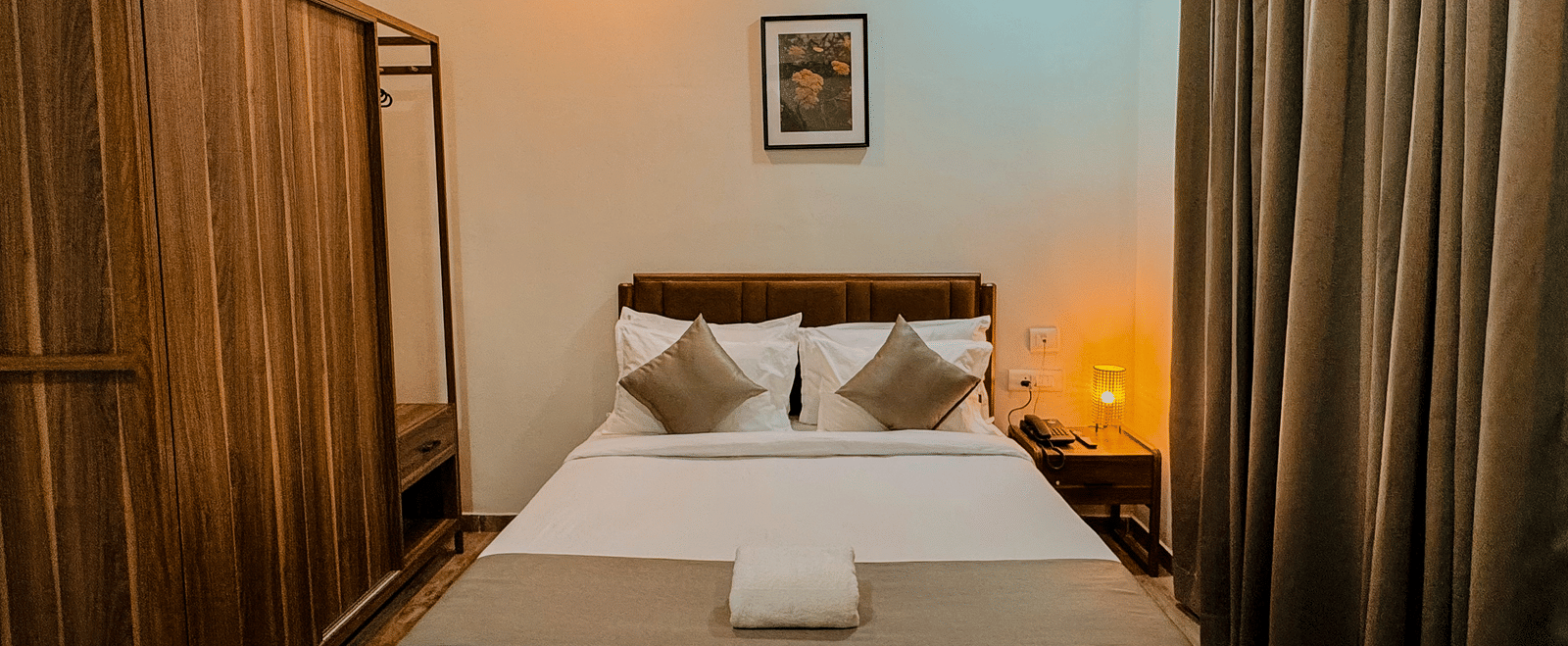 Furnishings including the queen size bed, a wooden wardrobe, and a bedside table seen in the bedroom of Coral 4BHK at Kove Smart Stays.