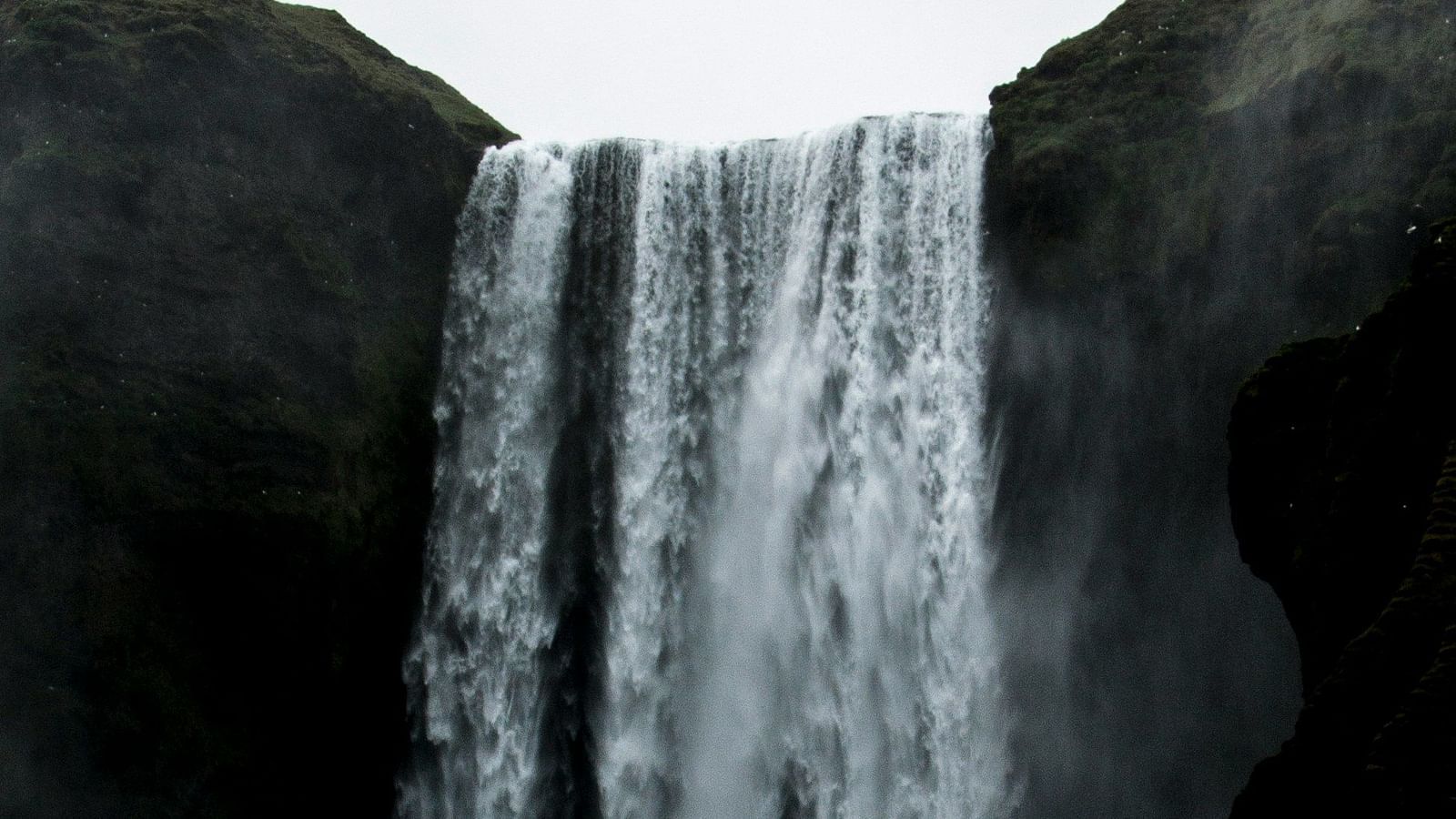 A waterfall cascading from a mountain with dark clouds covering the sky