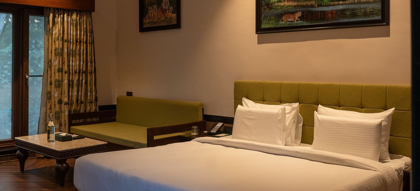 A well-appointed room at Aamaghati Jungle Retreat, Ranthambore, showcasing a bed with crisp white linens, a comfortable sofa, and framed artwork.