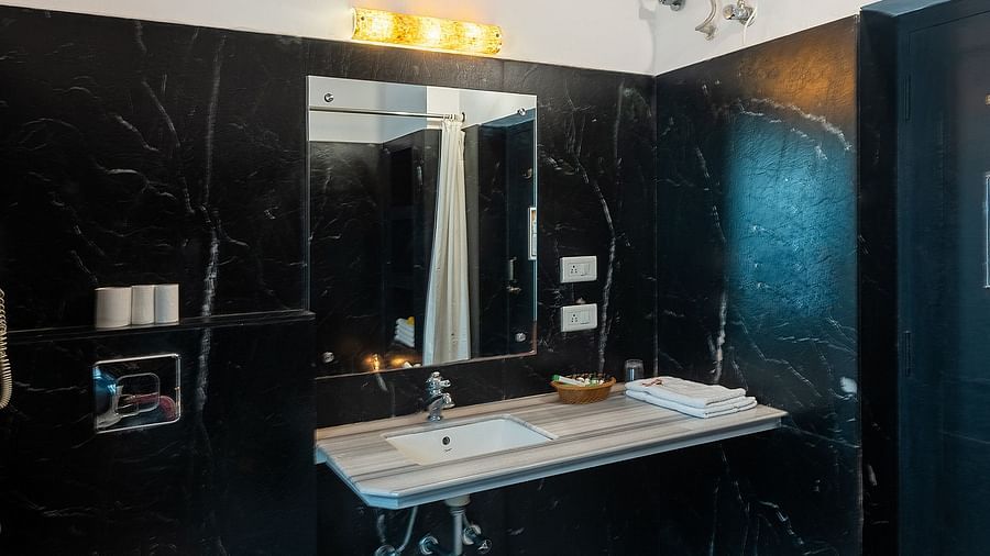 A bathroom featuring a wall-mounted mirror above a washbasin, with a western toilet positioned to the side  | Panna Vilas Udaipur