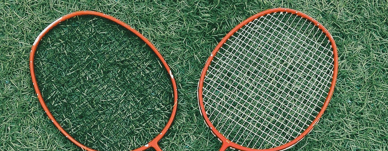 Top view of two badminton raquets, two shuttles and a water bottle on a grass surface.