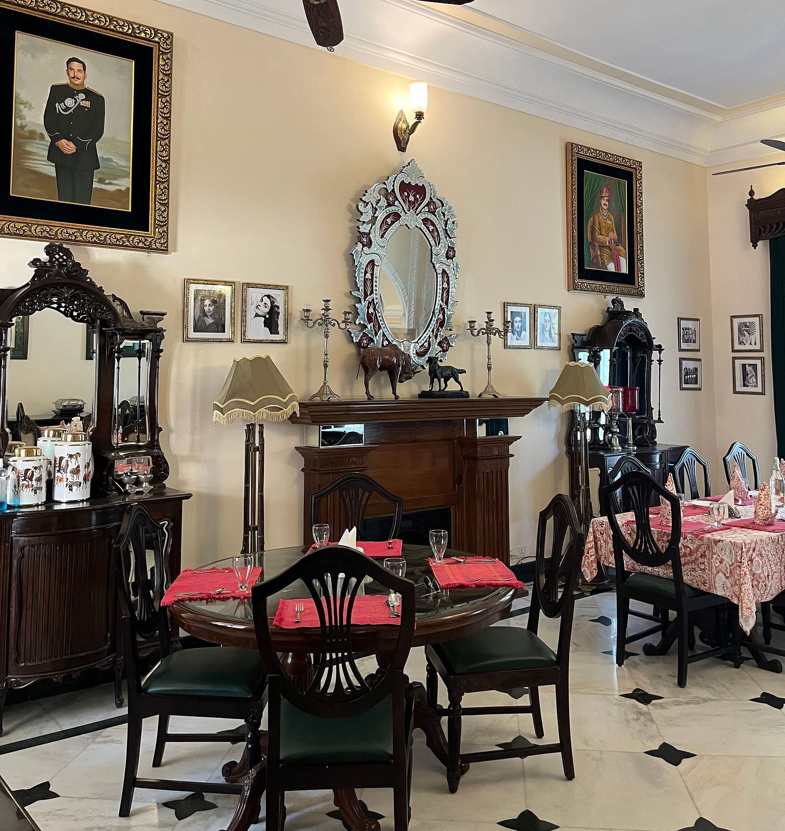  A room with traditional decor, featuring a ceiling fan, framed portraits, and dining tables - Khas Bagh, Jaipur.