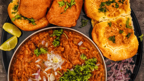 A plate of pav bhaji served with bread rolls, onions, lemon slices, and chutney.