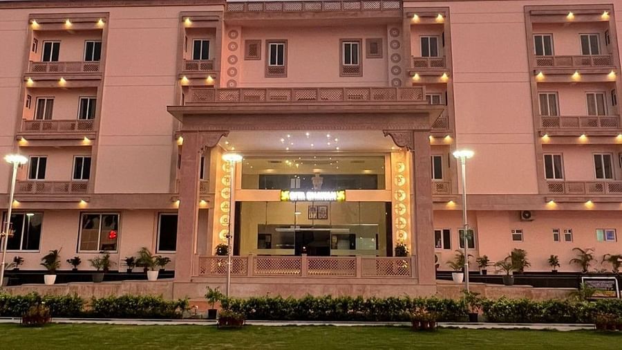 The front of a grand, light-pink building with an ornate entrance is illuminated in the evening - Kankidham Lords Inn
