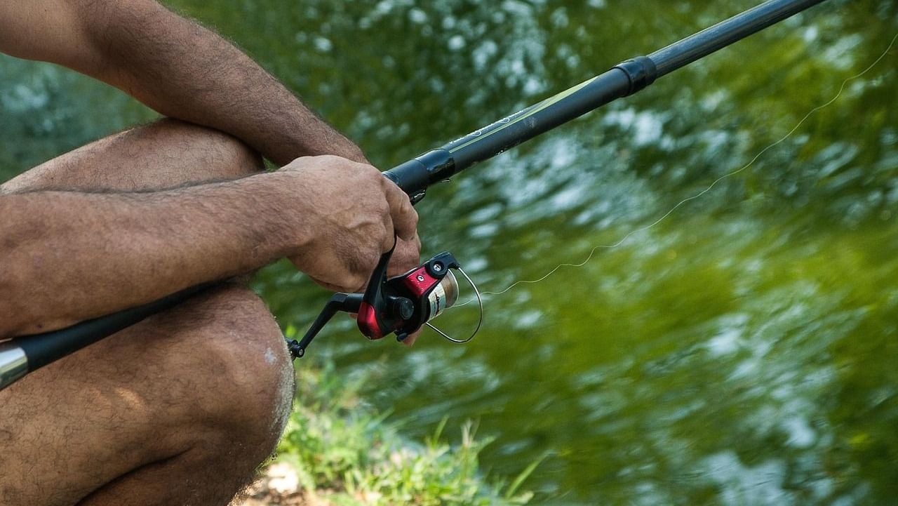 An angler sitting by the banks of a water body with the line cast in the water.