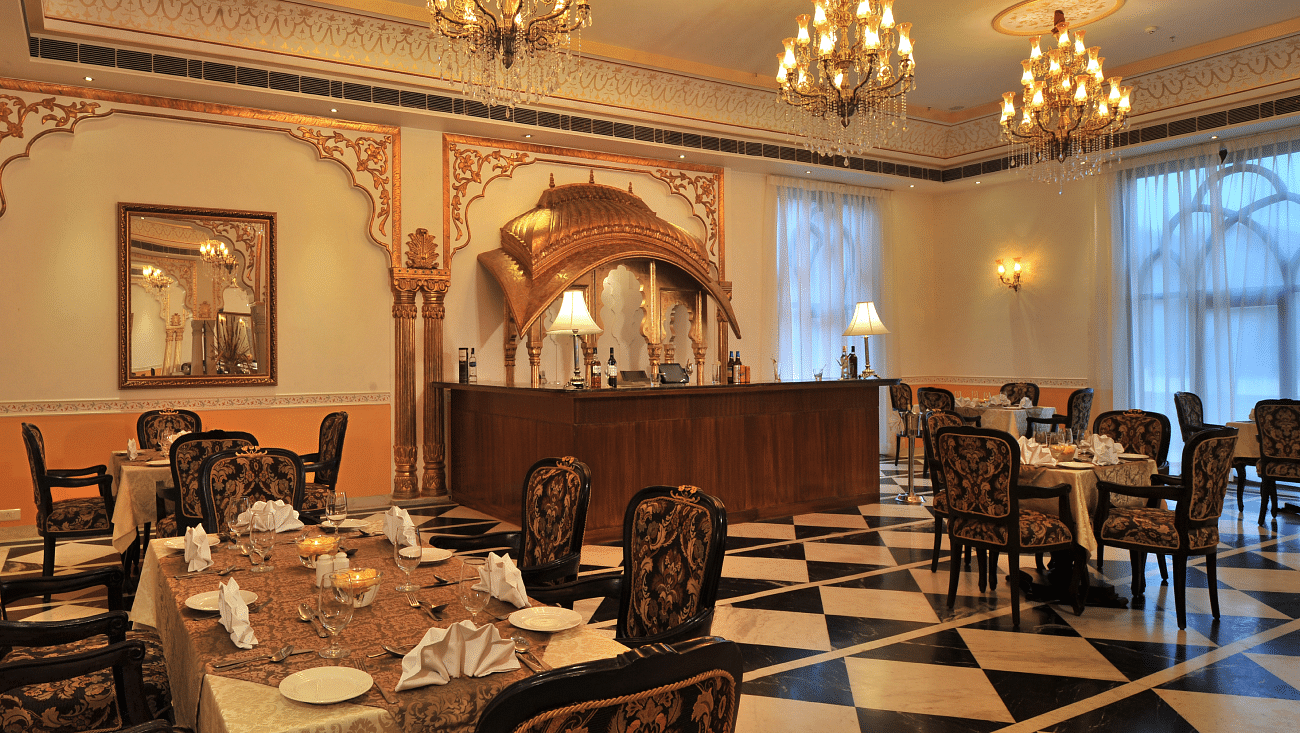 Dining area at Rajasthali Resort & Spa Jaipur with chairs, tables and chandeliers hanging from the ceiling.