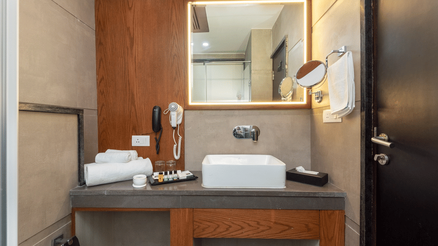 A modern bathroom at Quality Inn with a white basin, an illuminated mirror, and a hair dryer on the counter.