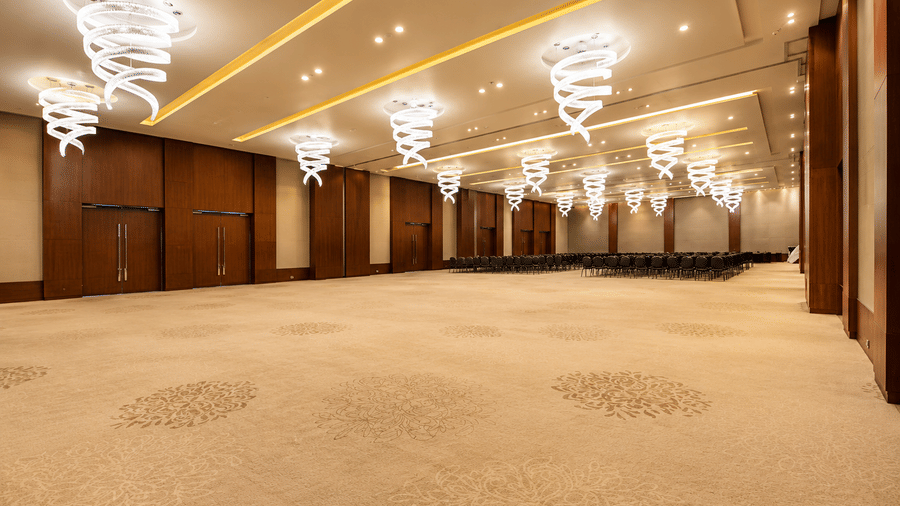 Spacious empty ballroom with carpeted flooring and spiral chandeliers at Kiranshree Grand Hotel.