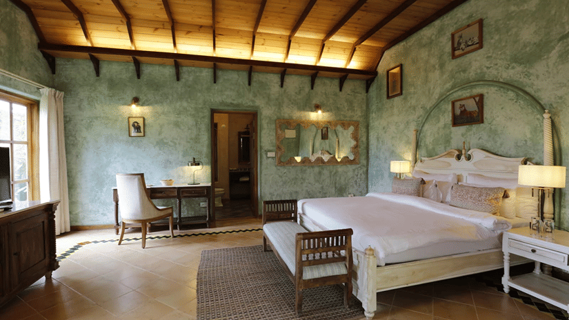 Guest room at Golden Tulip Goa, Mandrem Beach with a king-size bed, green textured walls, a wooden raftered ceiling, a writing desk, and a cushioned bench.