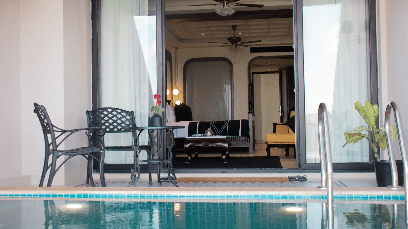 Luxurious and elegant room with large windows opening to a private swimming pool, complemented by a few chairs for a relaxing outdoor view