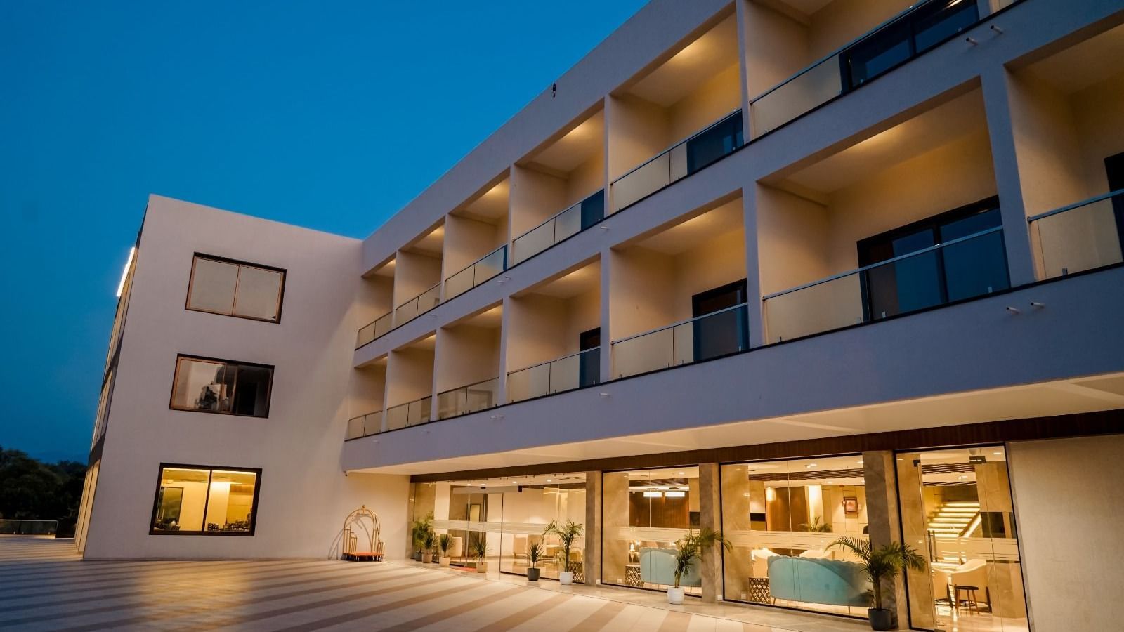 A nighttime exterior view of the Arawali Ananta Elite Jaipur hotel building with lights on and a swimming pool visible in the foreground.
