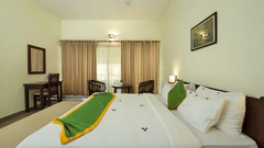 A bedroom features two beds with a green accent and artwork on the wall.- Abad Brookside Lakkidi, Wayanad