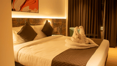 A hotel bedroom with king size bed, pillows, bedside lighting, and folded towel decor on the bed.