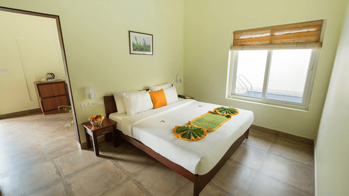 A bedroom features a neatly made-up bed with side tables, indicating a comfortable and well-prepared space. - Abad Brookside Lakkidi, Wayanad