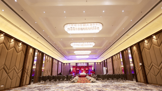 A perspective shot of a large, empty ballroom at Pride Premier Alwar, highlighting the expansive marble flooring, decorative ceiling light fixtures, and modern geometric wall designs.