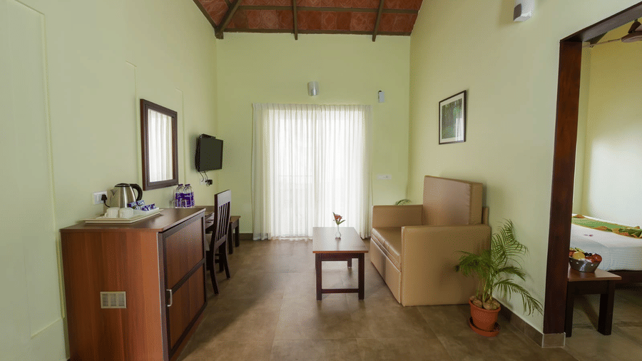 A living area features a wooden cabinet and a doorway leading to another room.- Abad Brookside Lakkidi, Wayanad