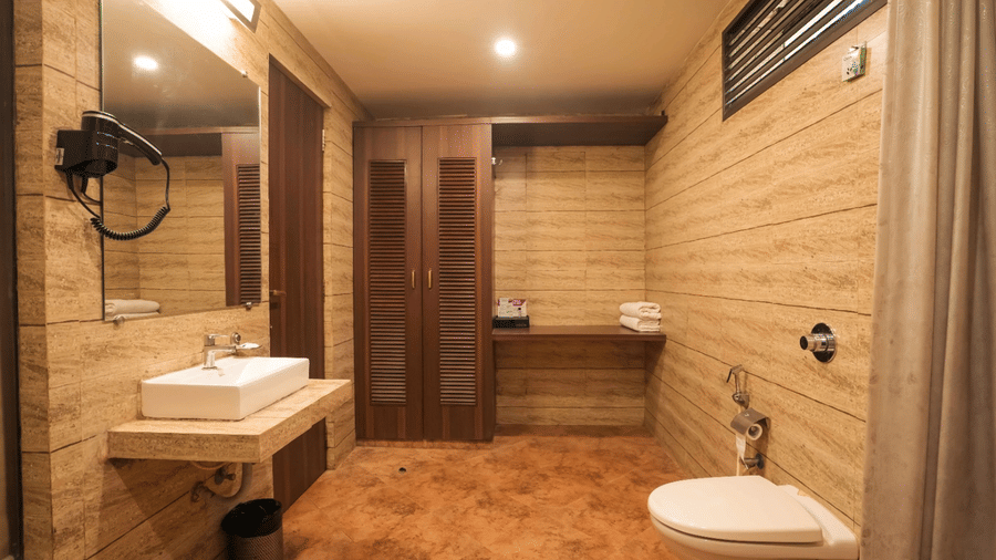 A well-lit washroom at Adamo The Village with a large wall mounted mirror and modern furnishing.