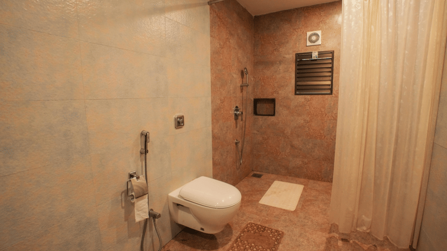 Interior view of Adamo The Village bathroom with a wall-mounted toilet, a curtain separating the shower area, and simple wall finishes.