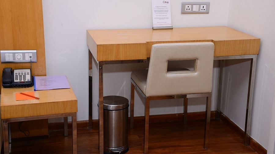 Hotel room workspace with wooden desk, cushioned chair, telephone, notepad, power outlet, and a stainless steel bin - Citrus Classic, Outer Ring Road, Bangalore
