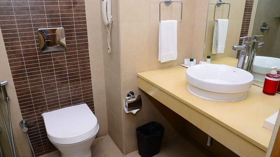 Modern hotel bathroom with wall-mounted toilet, round countertop sink, mirror, towel rack, and toiletries on the counter - Citrus Classic, Outer Ring Road, Bangalore