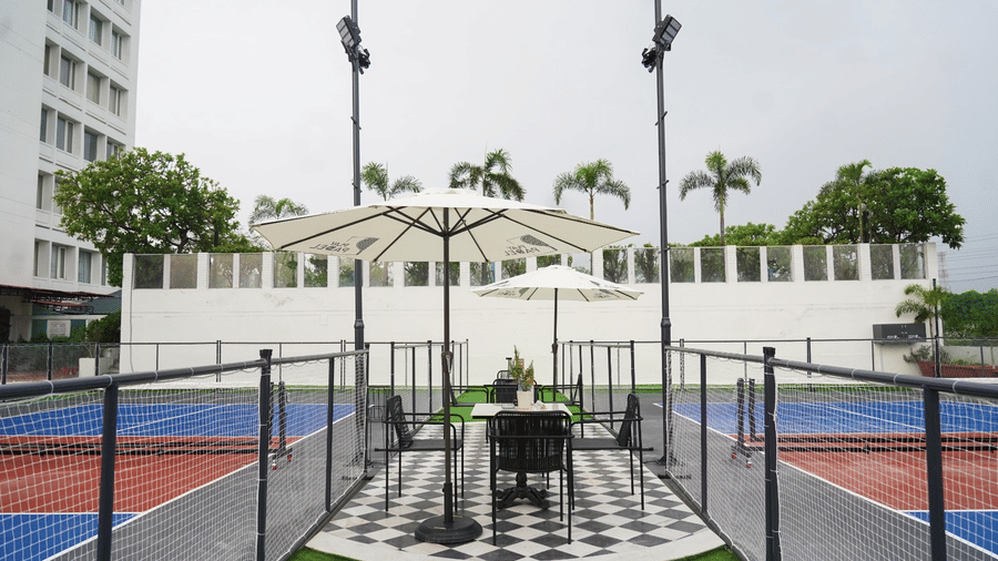 A multi-sport outdoor court with net fencing, central seating structure, overhead lighting poles, and surrounding buildings at Clarks Avadh, Lucknow.