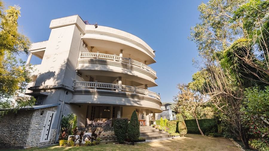 A unique, curvilinear white building at Saffron Leaf W567 A Luxuary and Boutique Stay multiple levels, surrounded by greenery under a clear sky, showcasing modern architecture.
