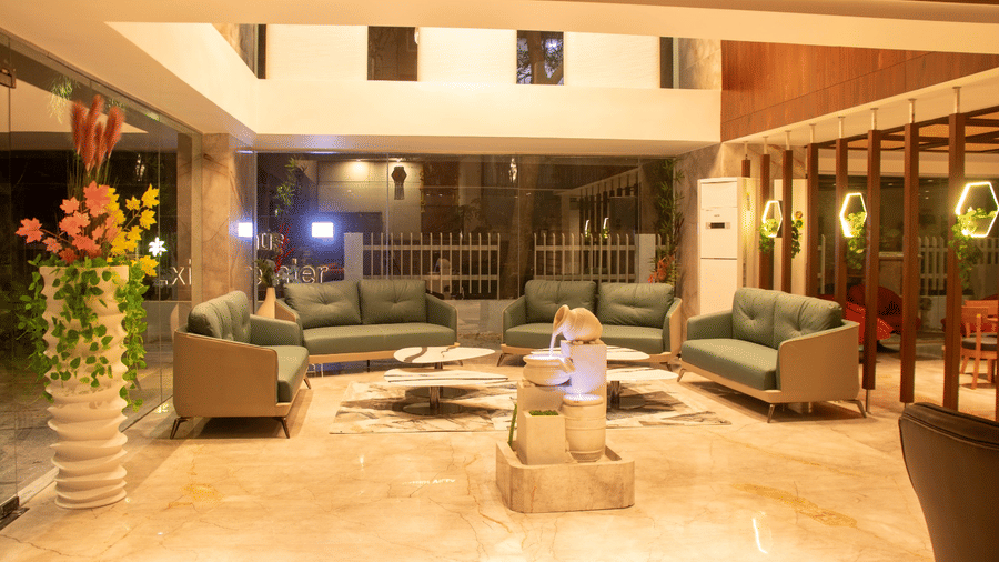 A hotel lobby with multiple sofas, center table, plants, and reception area visible in the background.