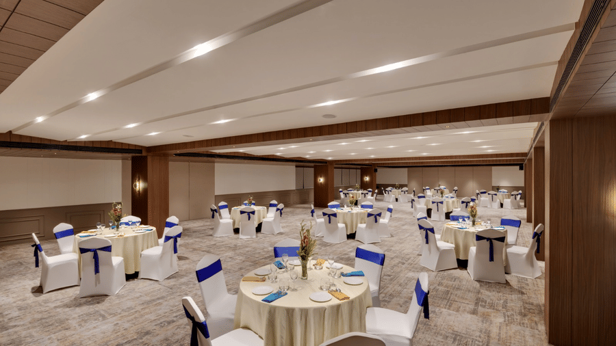 A  modern, well-lit banquet hall at the Voyage Milestone Hotel & Banquet, set up with round tables and chairs with sashes for an event.