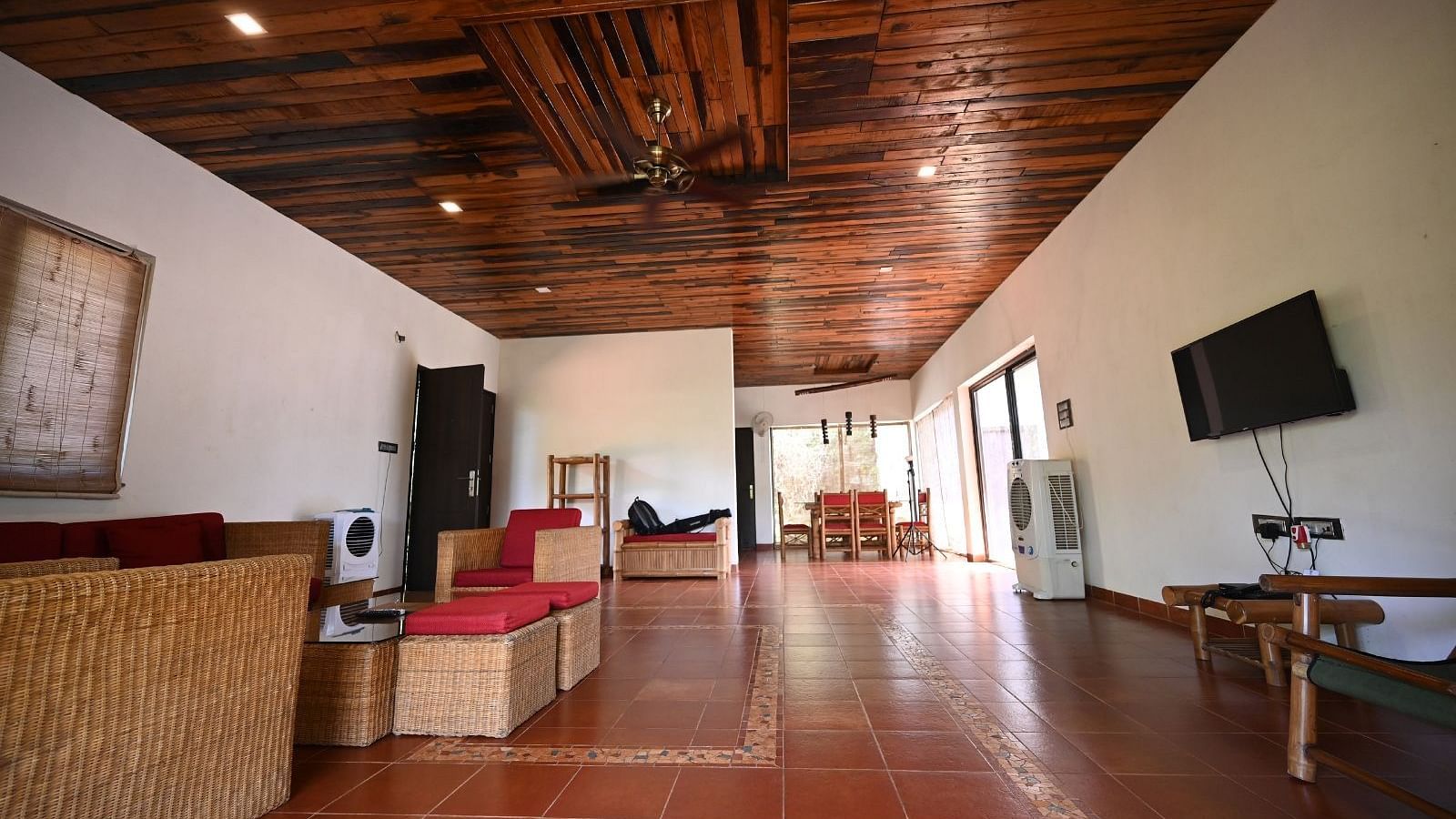 A long room with a wooden floor, tan furniture, and a television on the wall.