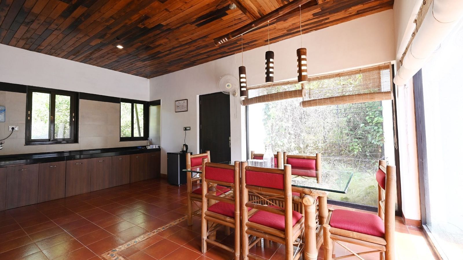 A room with a wooden floor, a red table and chairs, and large windows.