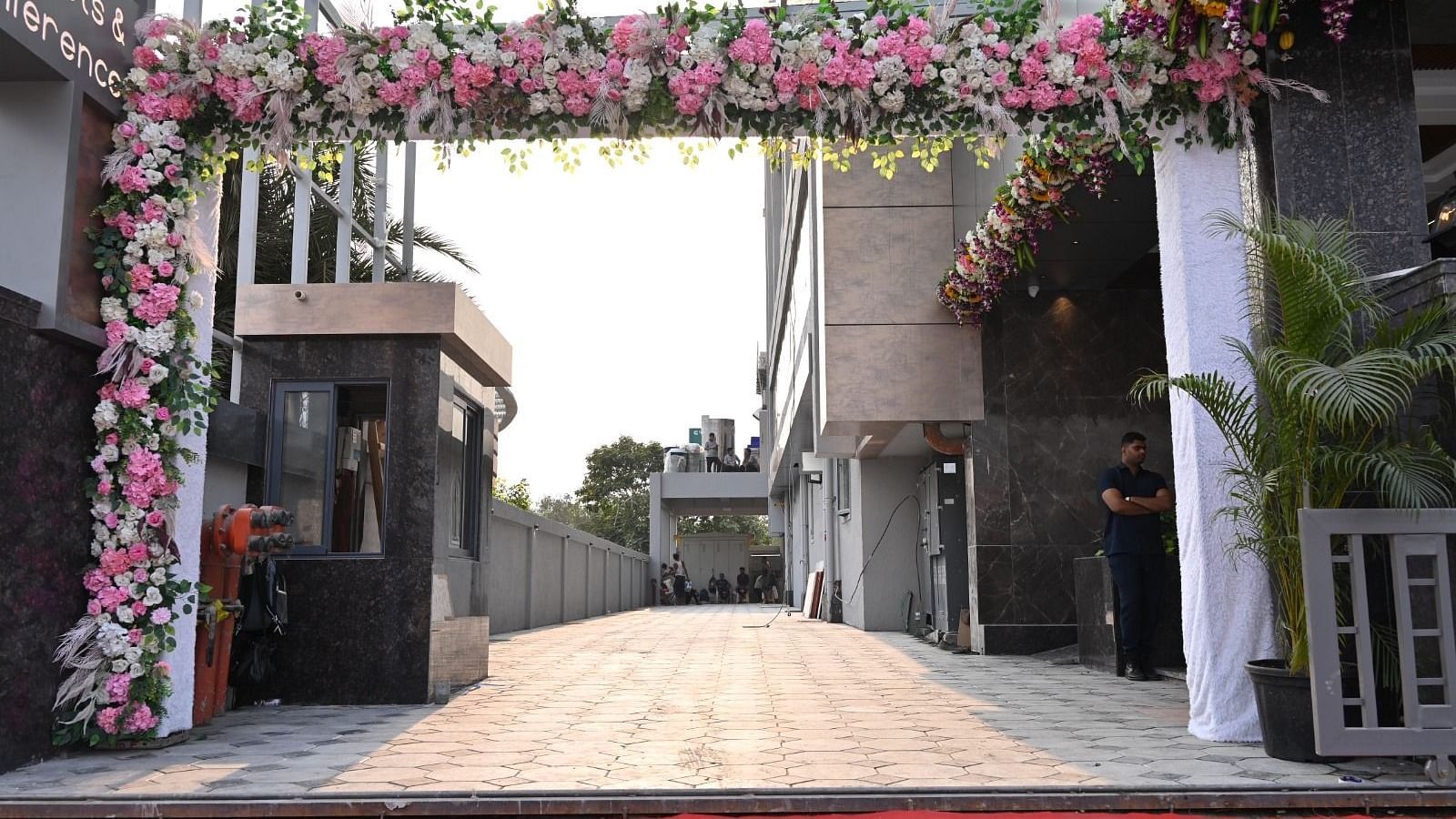 An outdoor entranceway decorated with flowers and lighting, leading towards a building under a bright sky - Melior Inn
