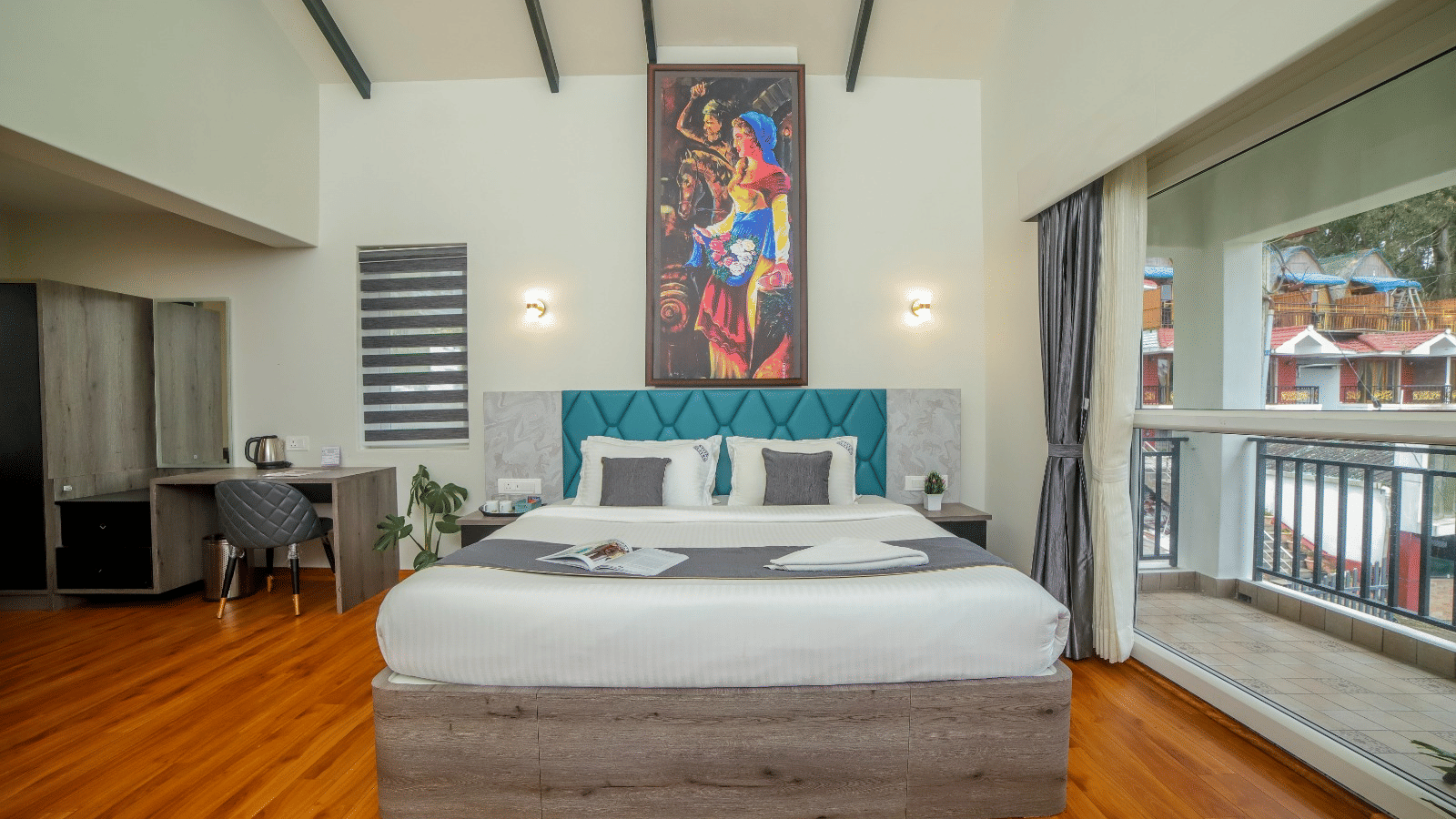 Brightly lit bedroom with a queen size bed, hardwood floor, desk, balcony access, and a tall artwork piece above the headboard | MYST Resorts, Doddabetta, Ooty