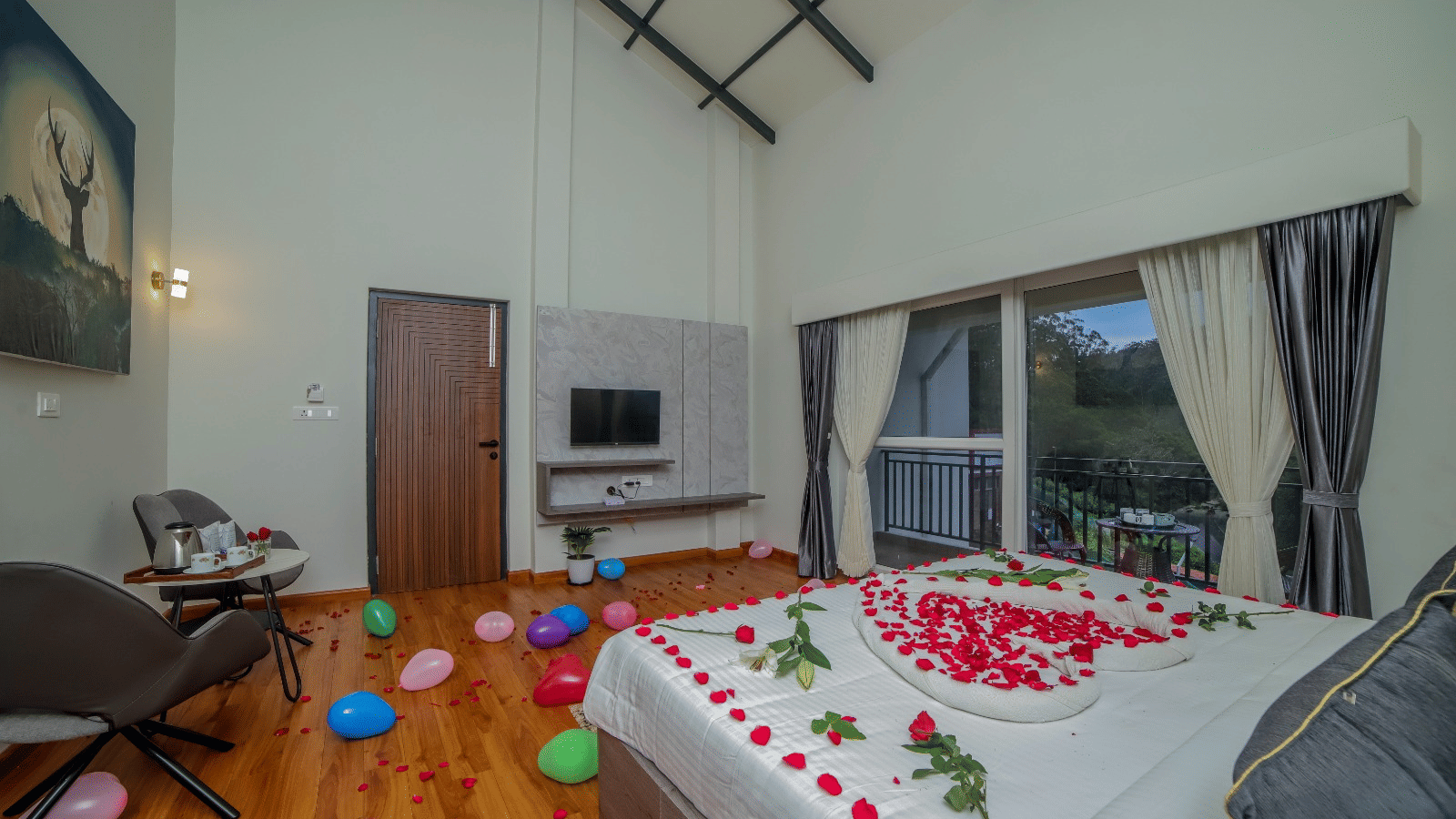 MYST Resorts bedroom with a high ceiling, hardwood floor, and a queen size bed decorated with rose petals in a heart shape, and balloons spread on the floor.