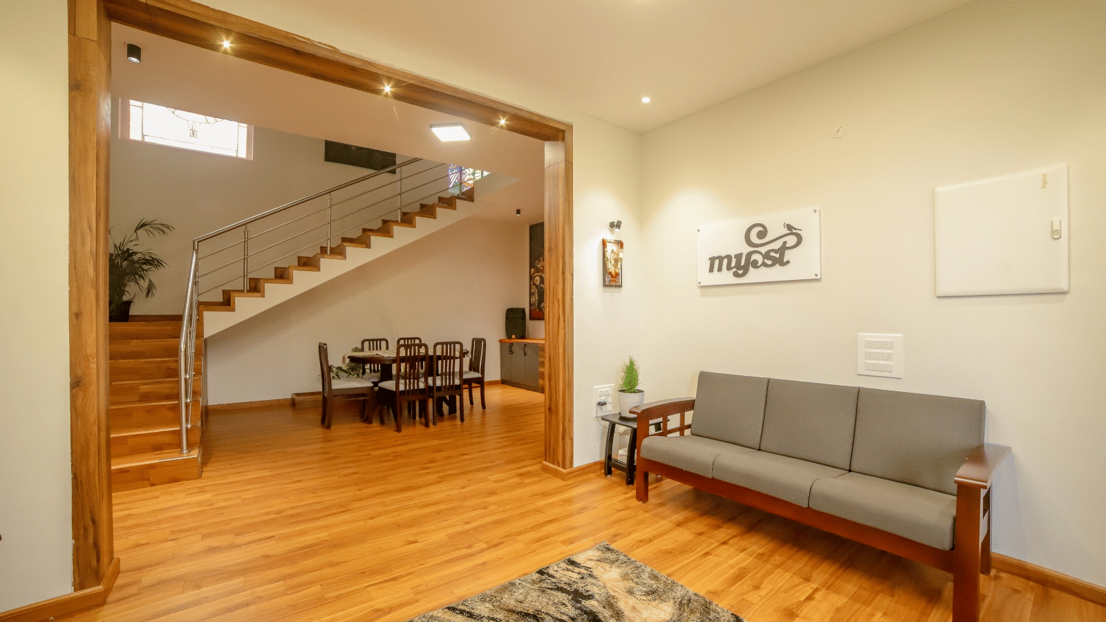 An upholstered multi-seater sofa seen in the living area of MYST Resorts, Doddabetta, Ooty, seen on wooden flooring, and the dining table seen in another section of the villa.