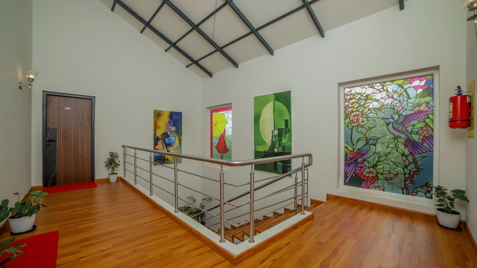 Common walkway on the upper floor of MYST Resorts, Doddabetta, Ooty, featuring potted plants, a railed staircase leading down, and a doorway to an upper-floor bedroom.