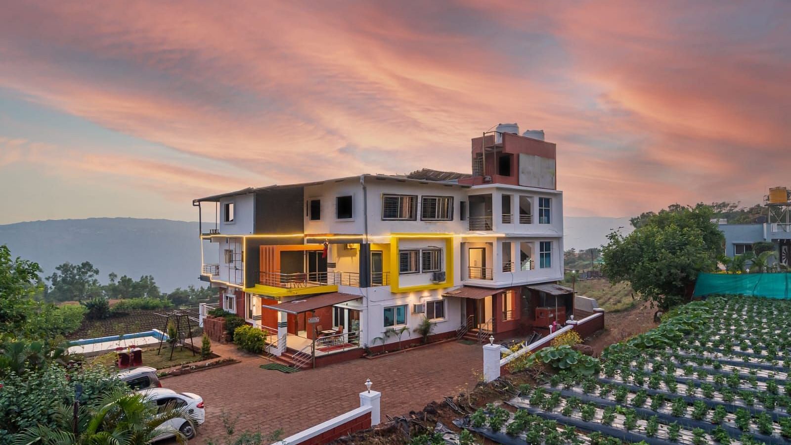 An exterior view of Strawberry King Resort, Mahabaleshwar at dusk surrounded by trees.