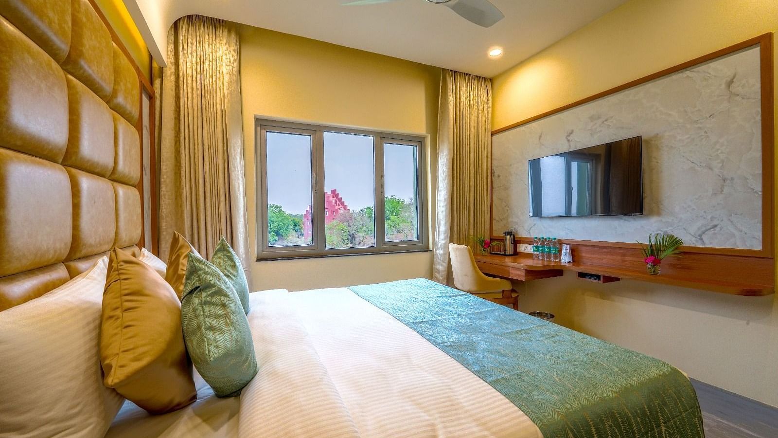 Bright and airy hotel room with a plush queen-sized bed, wooden accents, and a view of the greenery outside Tara, Comfort Hotel in Hyderabad - Ramoji Film City.