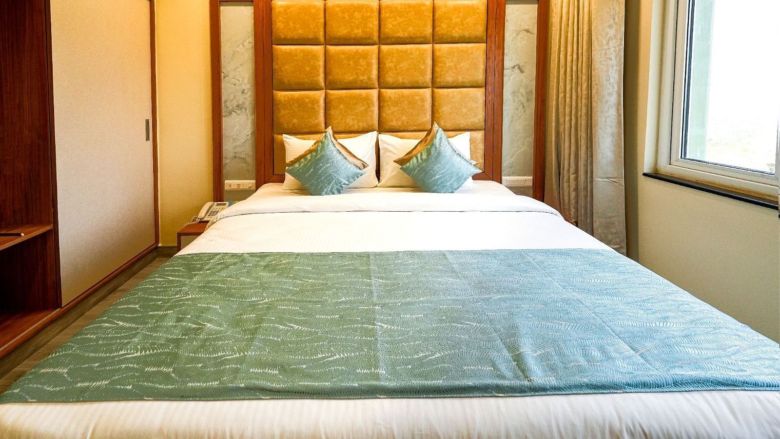 Inviting hotel room with a neatly made bed, cushioned headboard, and a view through the large window Tara, Comfort Hotel in Hyderabad - Ramoji Film City.