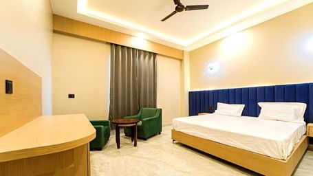 Modern guest room at Grassfield Riveria Resort, Jaipur, featuring a large bed, seating area, ceiling fan, and warm lighting.